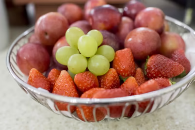 Obstschüssel mit Erdbeeren, Pflaumen und grünen Trauben 
